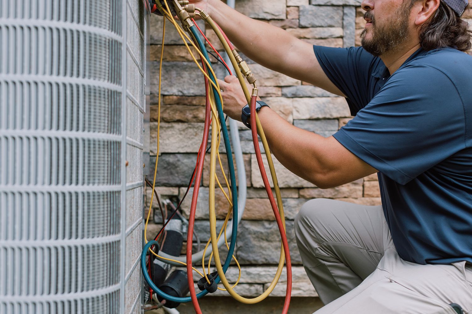 HVAC technician servicing an air conditioning unit outdoors, connecting refrigerant gauges to the system.