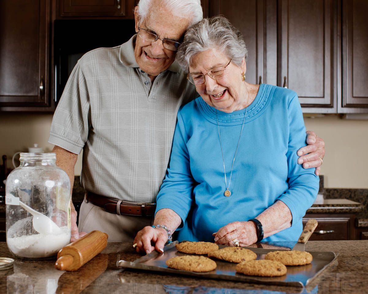 Elderly couple laughing together while baking cookies in a cozy kitchen.
