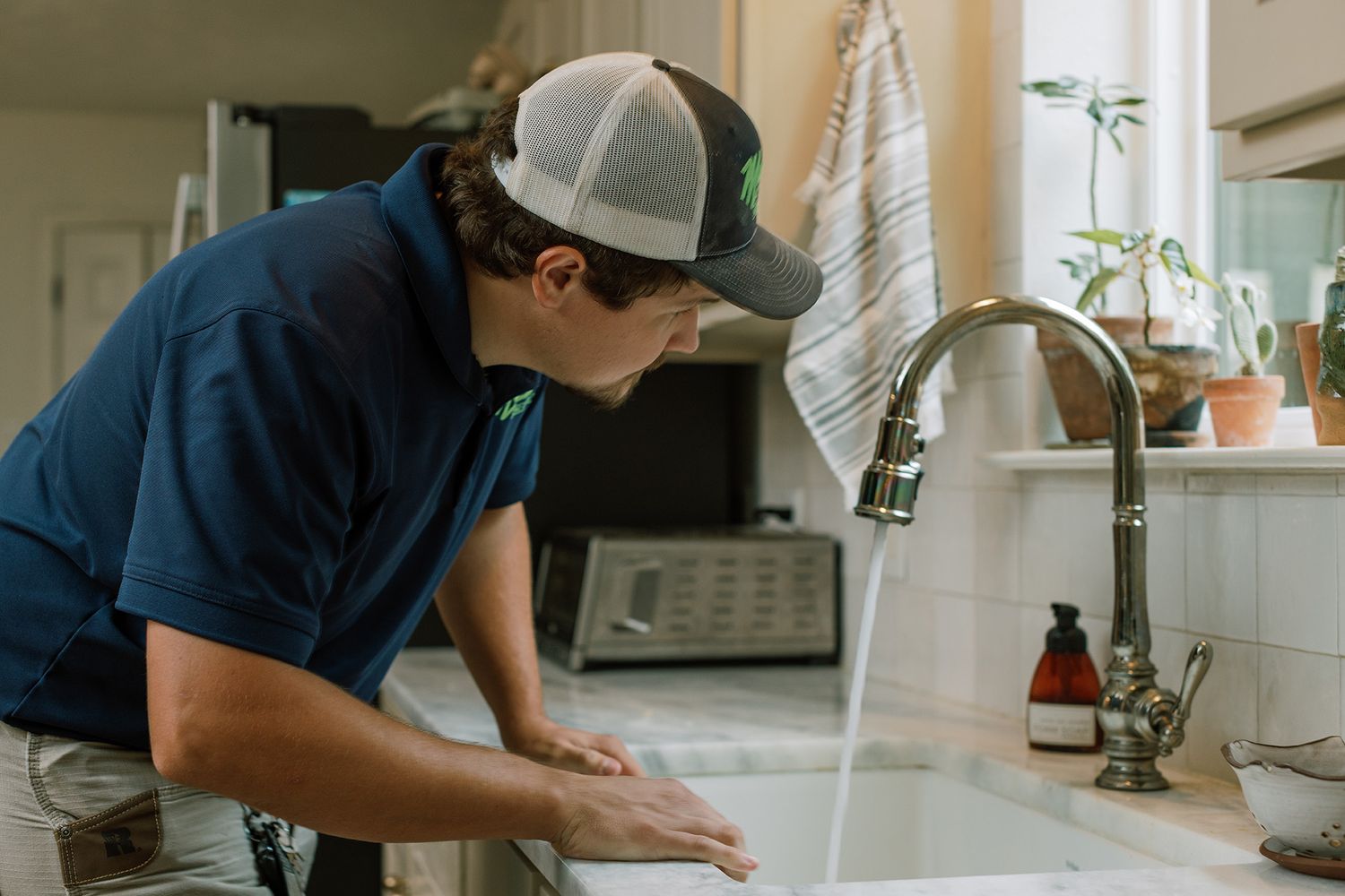 Malek plumber inspecting a kitchen sink faucet with running water during a service call.