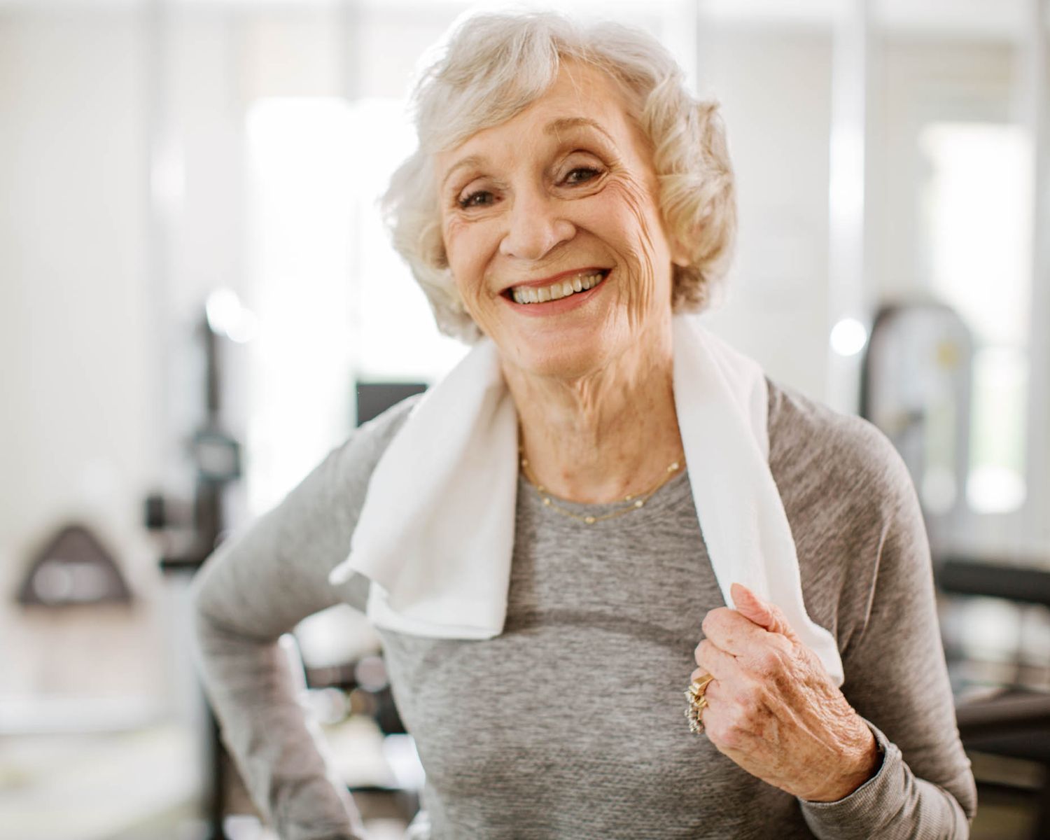Smiling senior woman with towel around neck after workout at a bright gym.
