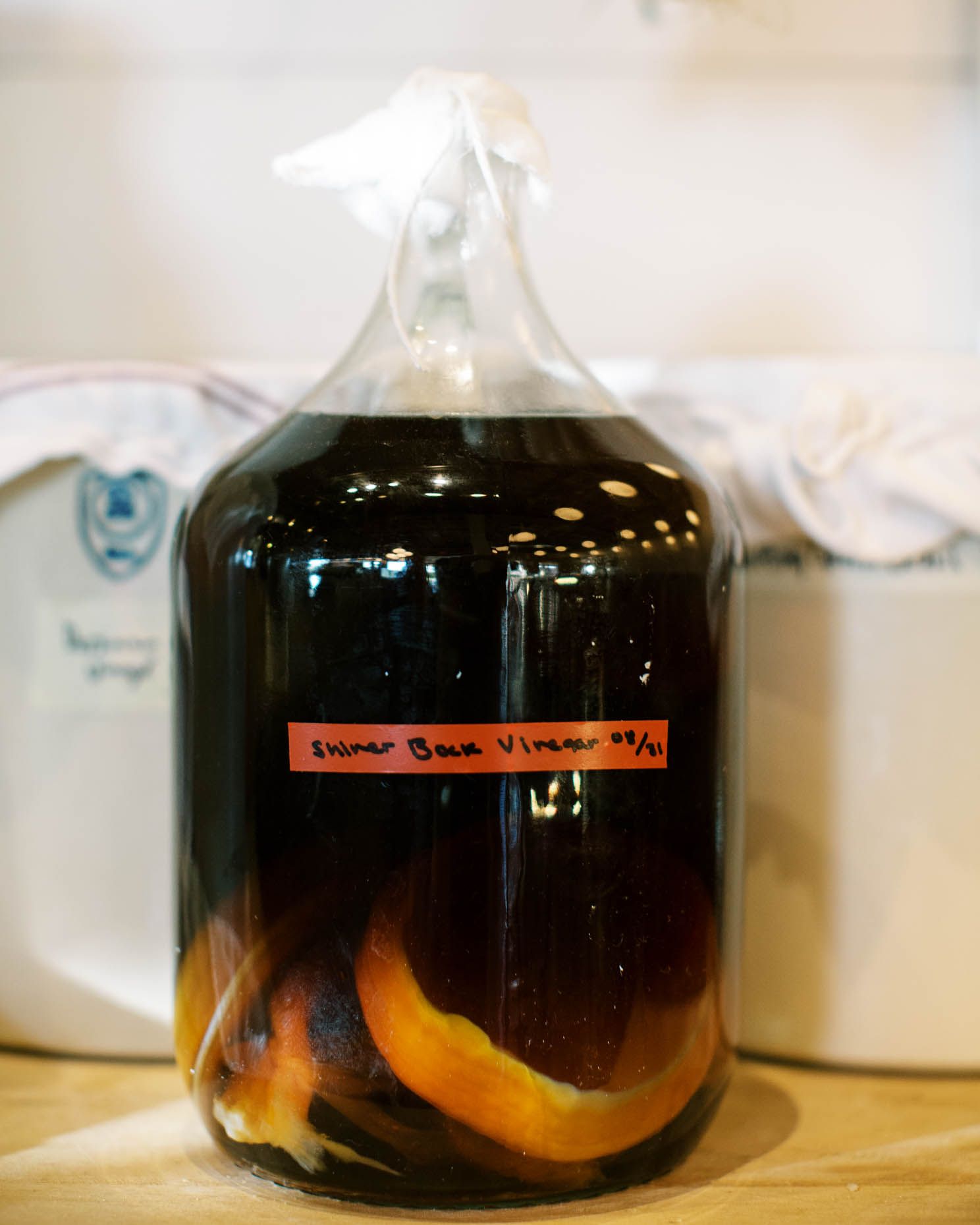 Glass jug of homemade Shiner Bock vinegar with orange peels, labeled and sealed with a cloth cover.