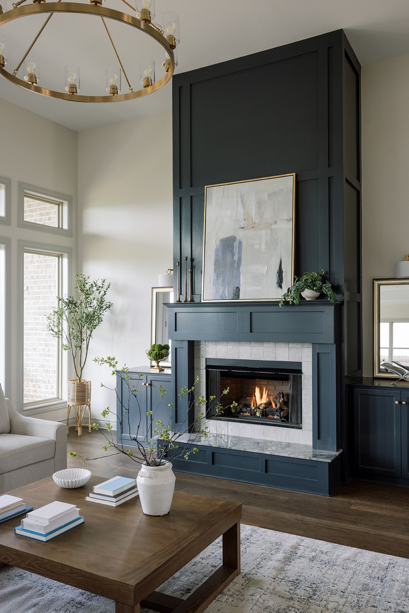 Dramatic dark navy fireplace surround with tall paneling, abstract art, gold chandelier, and wood coffee table.