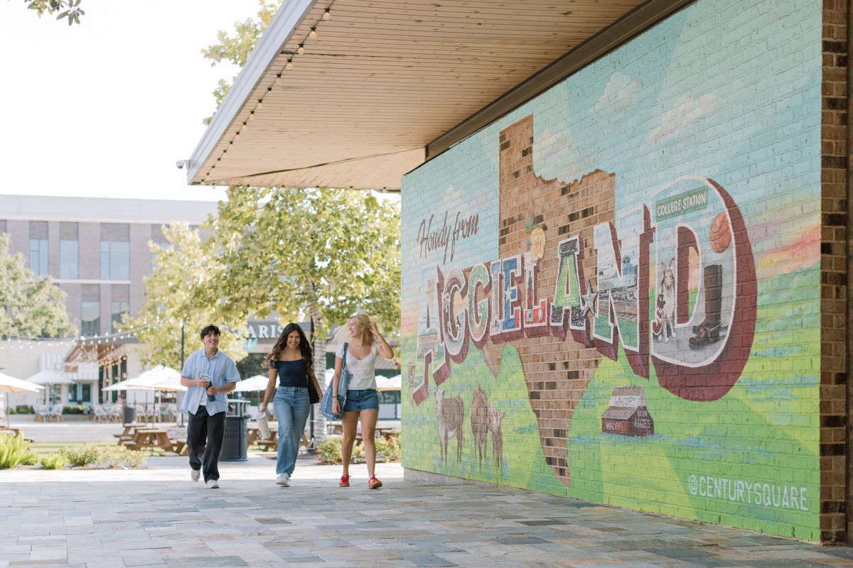 Students walk past a colorful Aggieland mural at a Texas A&M campus outdoor plaza.