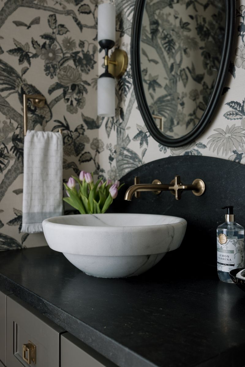 Dramatic powder room with botanical wallpaper, marble vessel sink, black vanity, and brass fixtures.