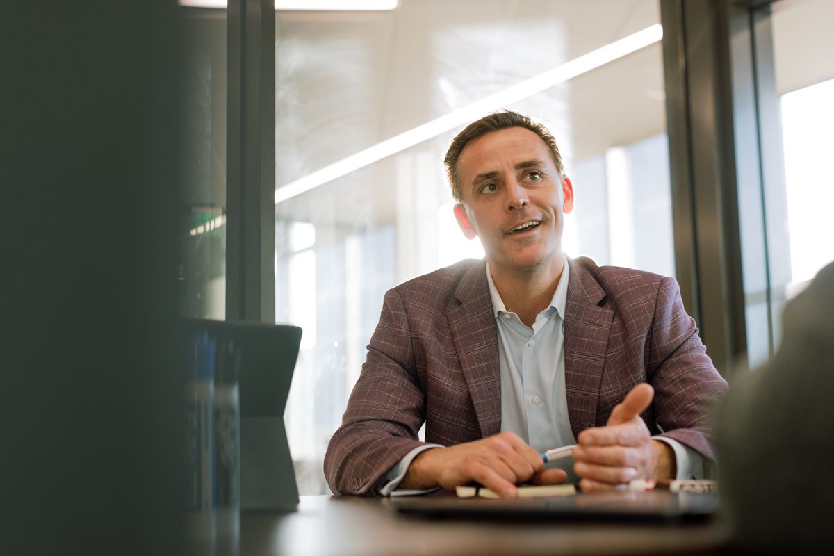 A professional man in a blazer sits at a conference table engaged in a business discussion.