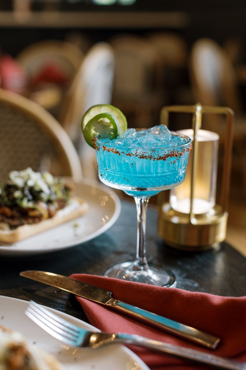 A vibrant blue margarita cocktail garnished with a lime slice and spiced rim, served in an elegant restaurant setting.