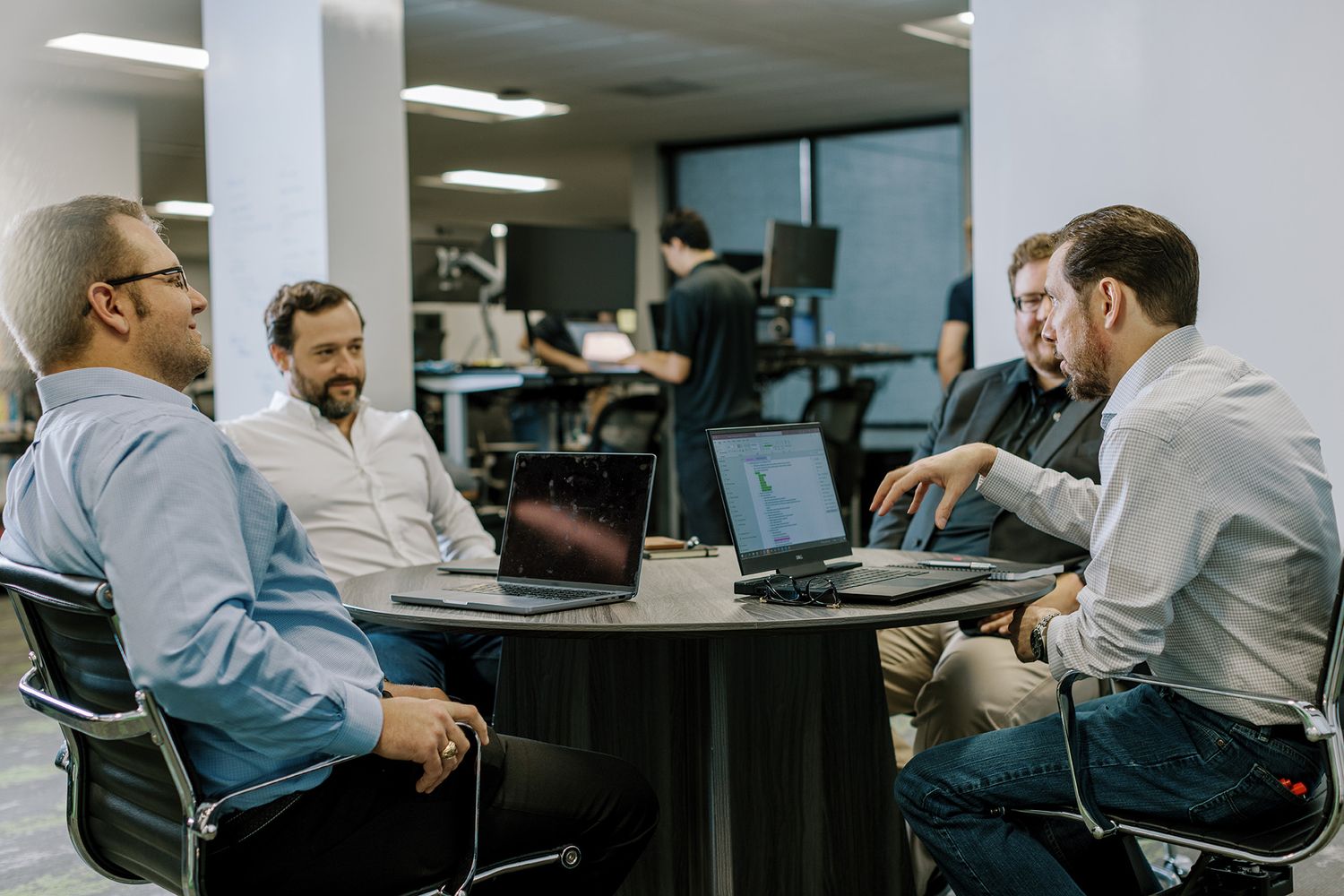 Four business professionals having a collaborative meeting around a round table with laptops in a modern office.