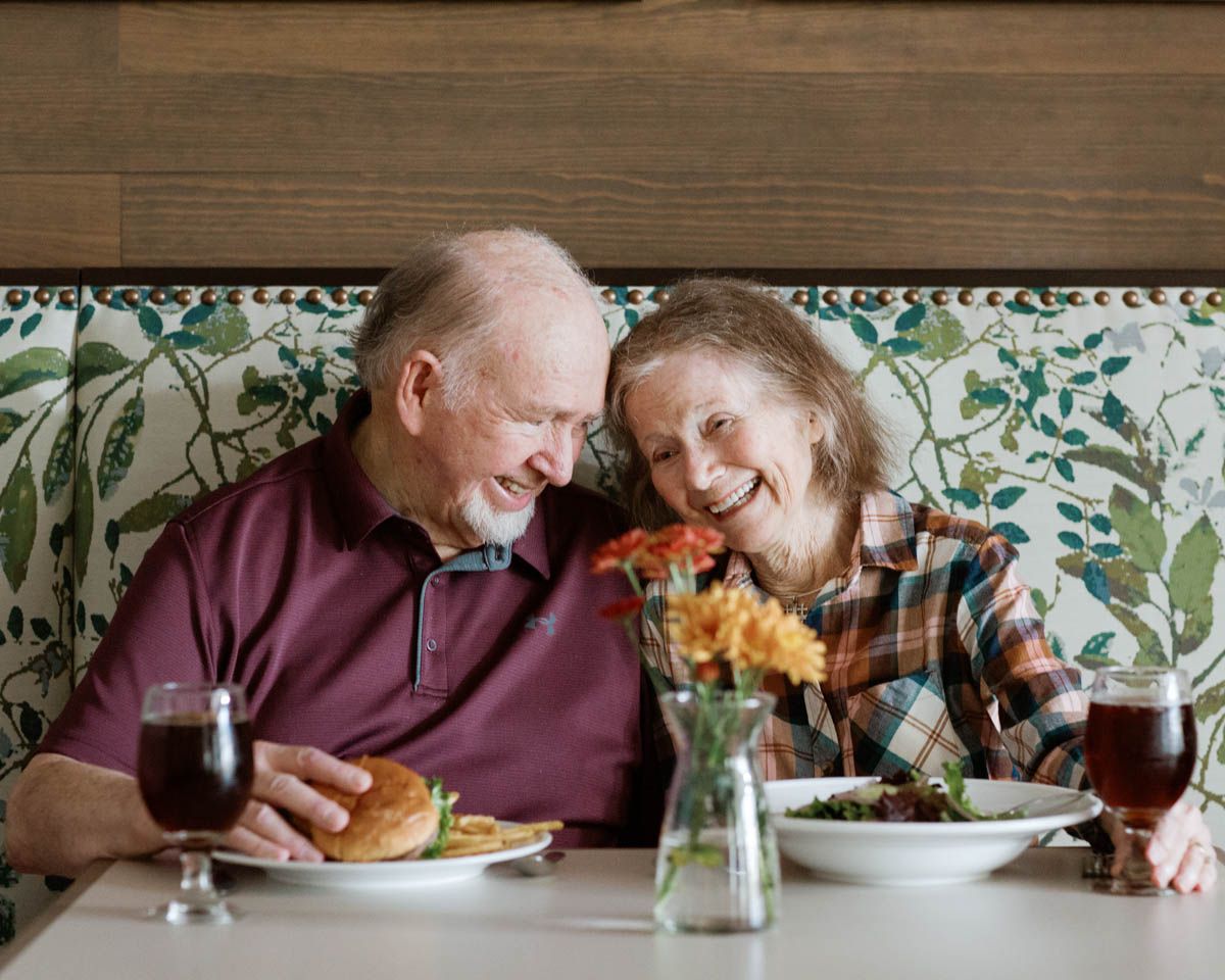 Elderly couple sharing a romantic dinner, laughing together over wine and food in a cozy restaurant booth.