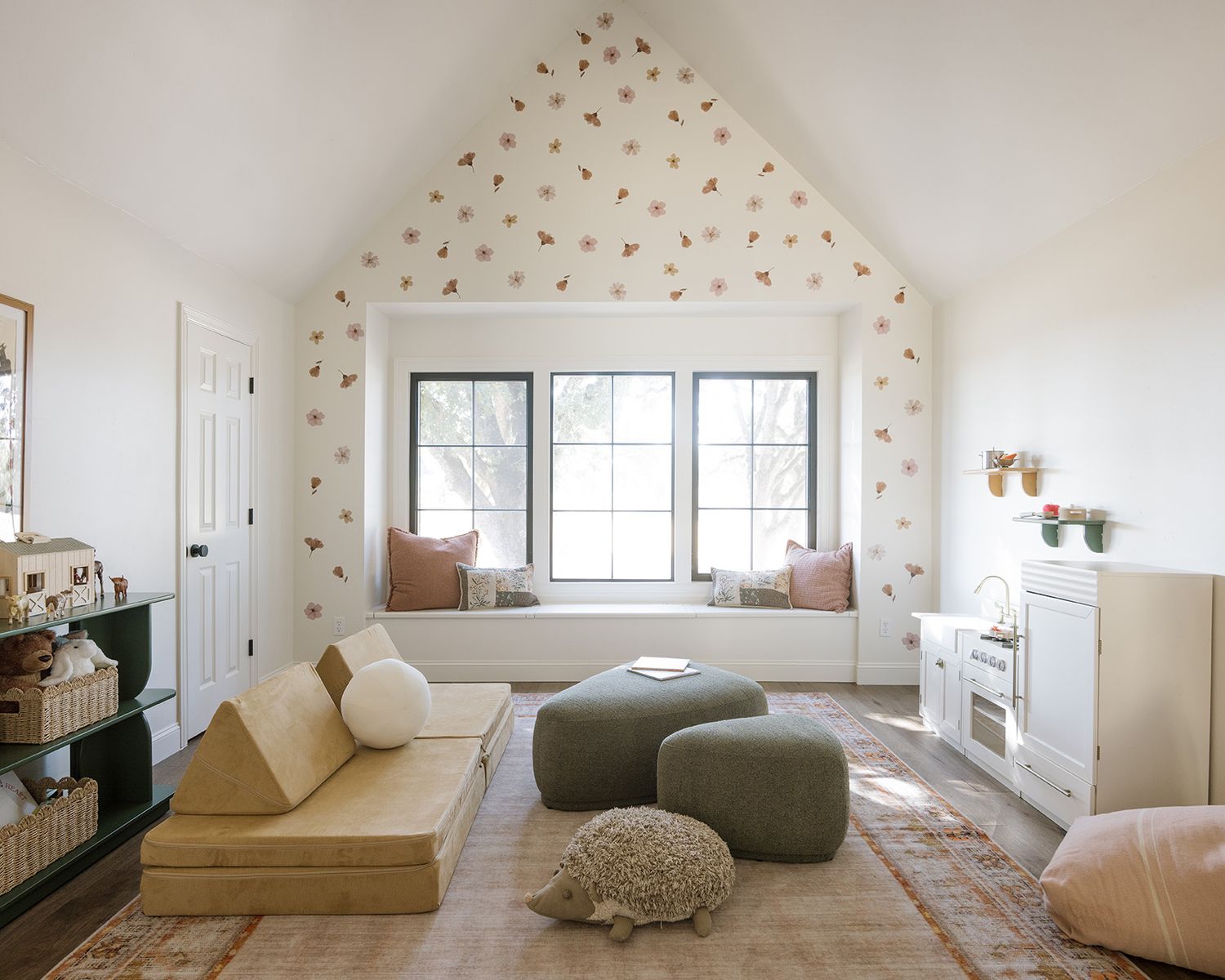 Bright playroom with vaulted ceiling, heart wallpaper, window seat, and soft floor cushions.
