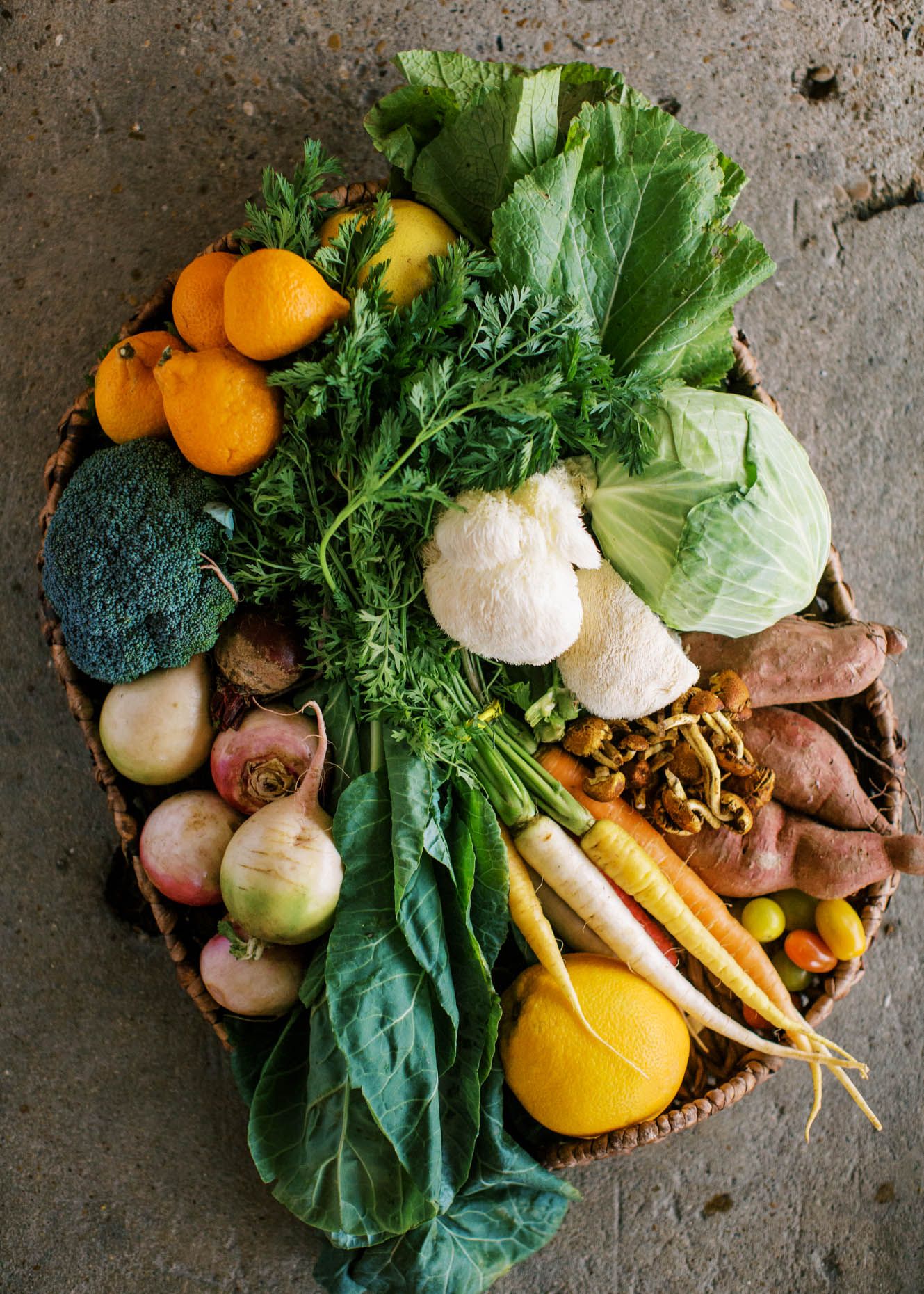 Overhead view of fresh seasonal vegetables in a wicker basket including carrots, cauliflower, and broccoli.