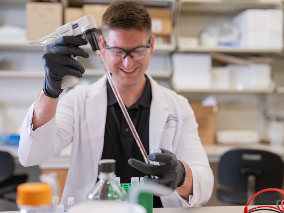 Young male scientist in white lab coat and safety glasses conducting experiment in laboratory.