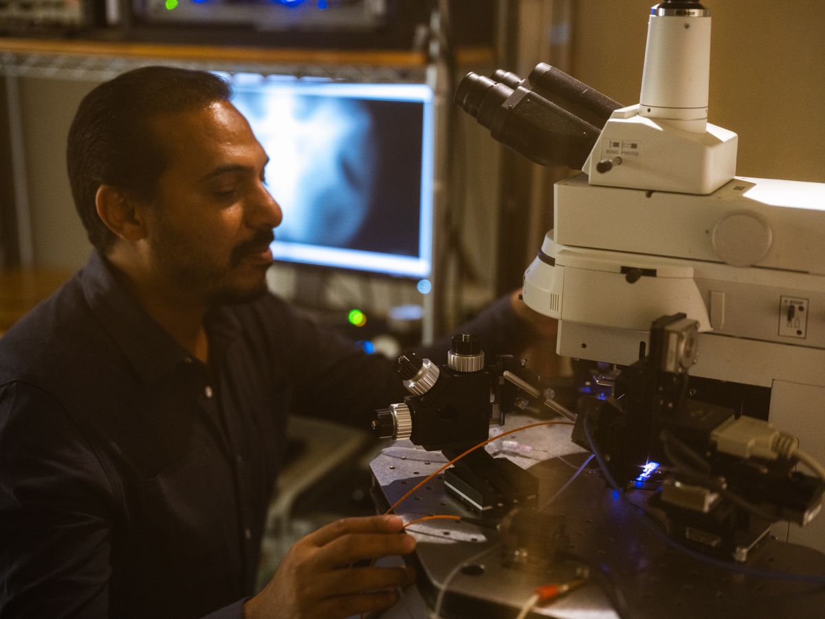 Male scientist examining samples under a microscope in a dark research laboratory setting.