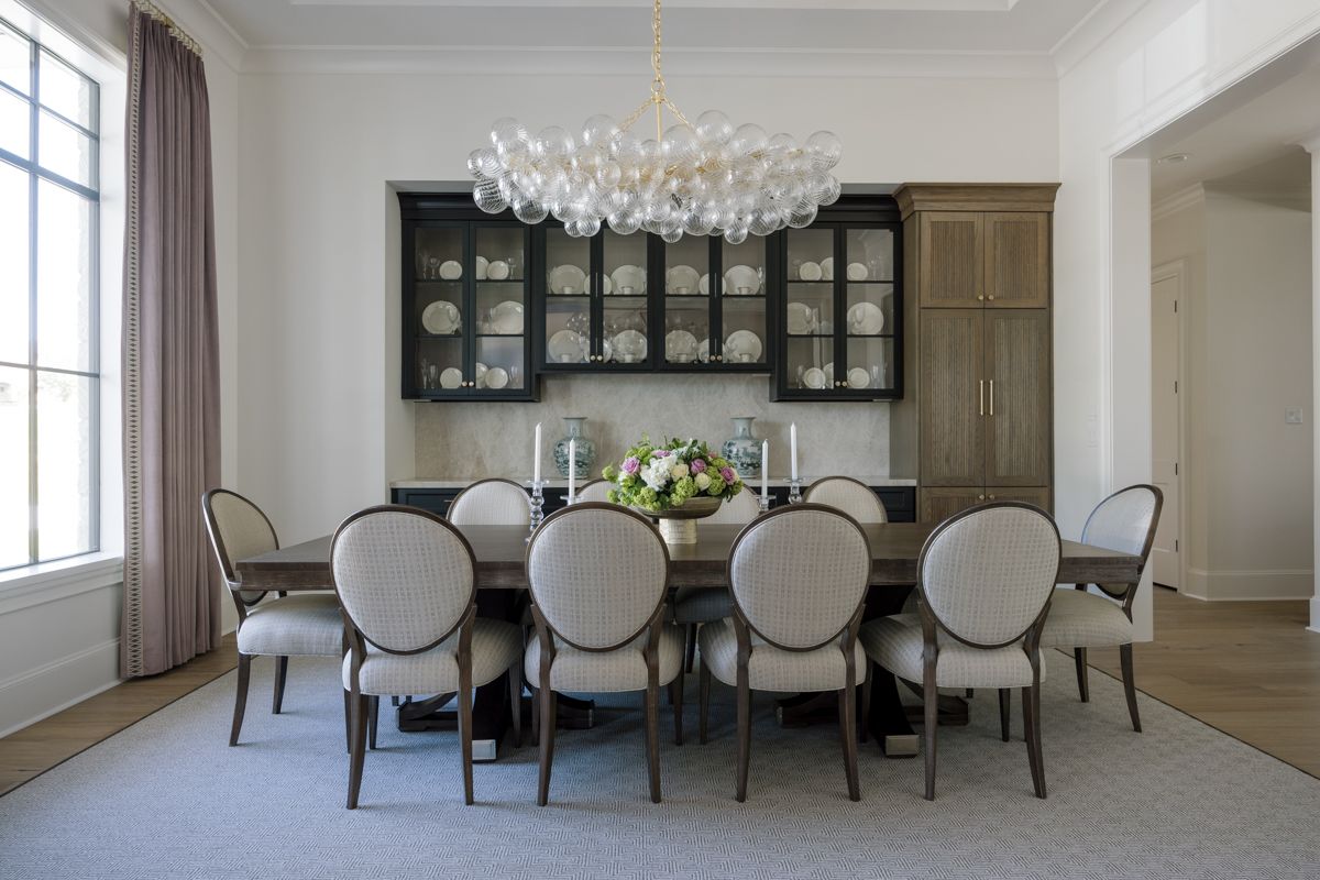 Elegant dining room with round-back chairs, dark wood hutch, floral centerpiece, and a white bubble chandelier.