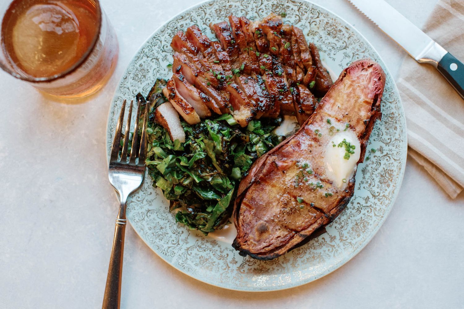 A restaurant plate with grilled steak, sautéed greens, and a stuffed lobster tail, served with a glass of beer.