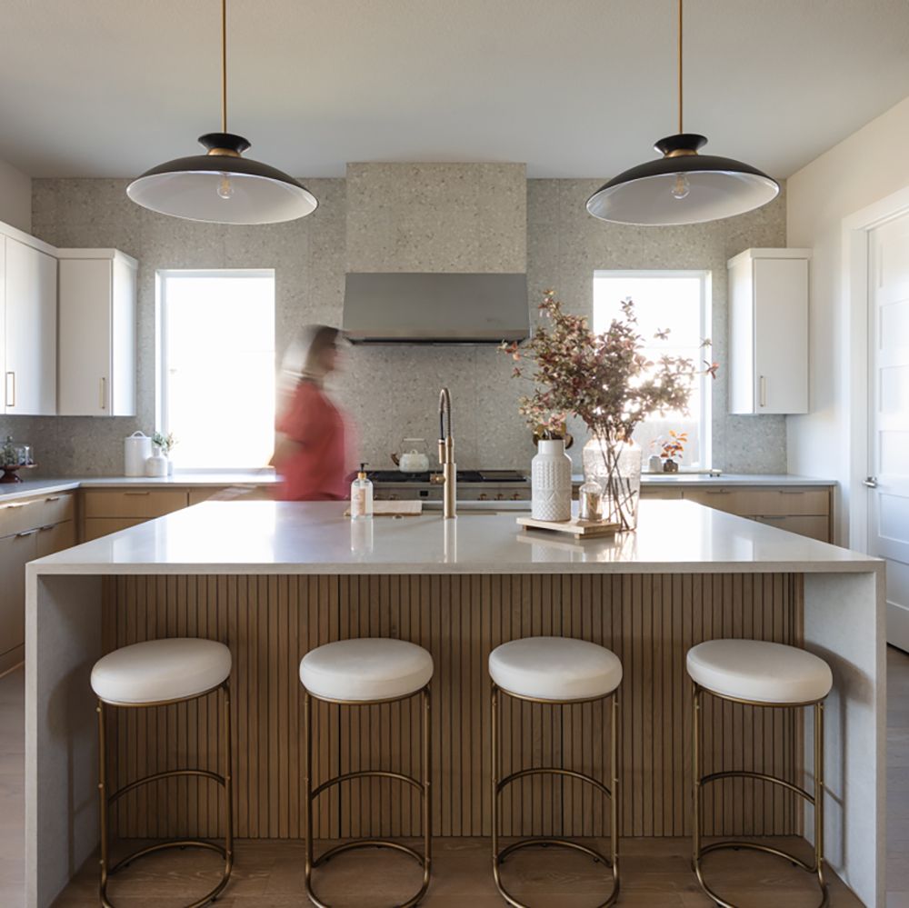 Modern kitchen with white island, bar stools, pendant lights, and person in motion near stainless steel range.