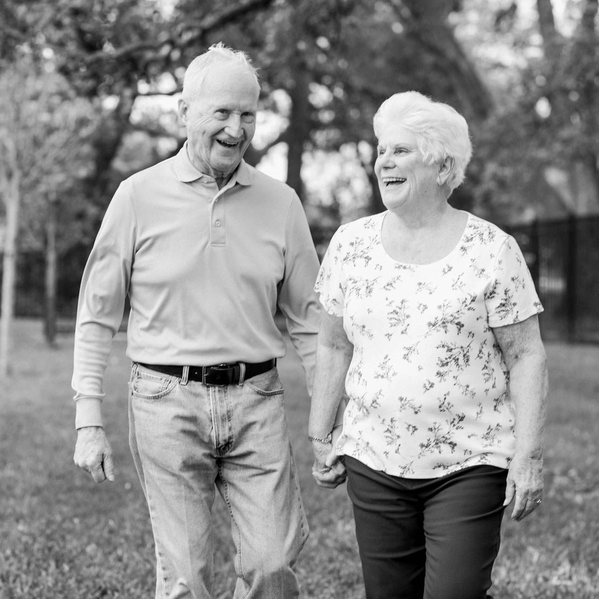 Elderly couple holding hands and smiling while walking together outdoors in a park.