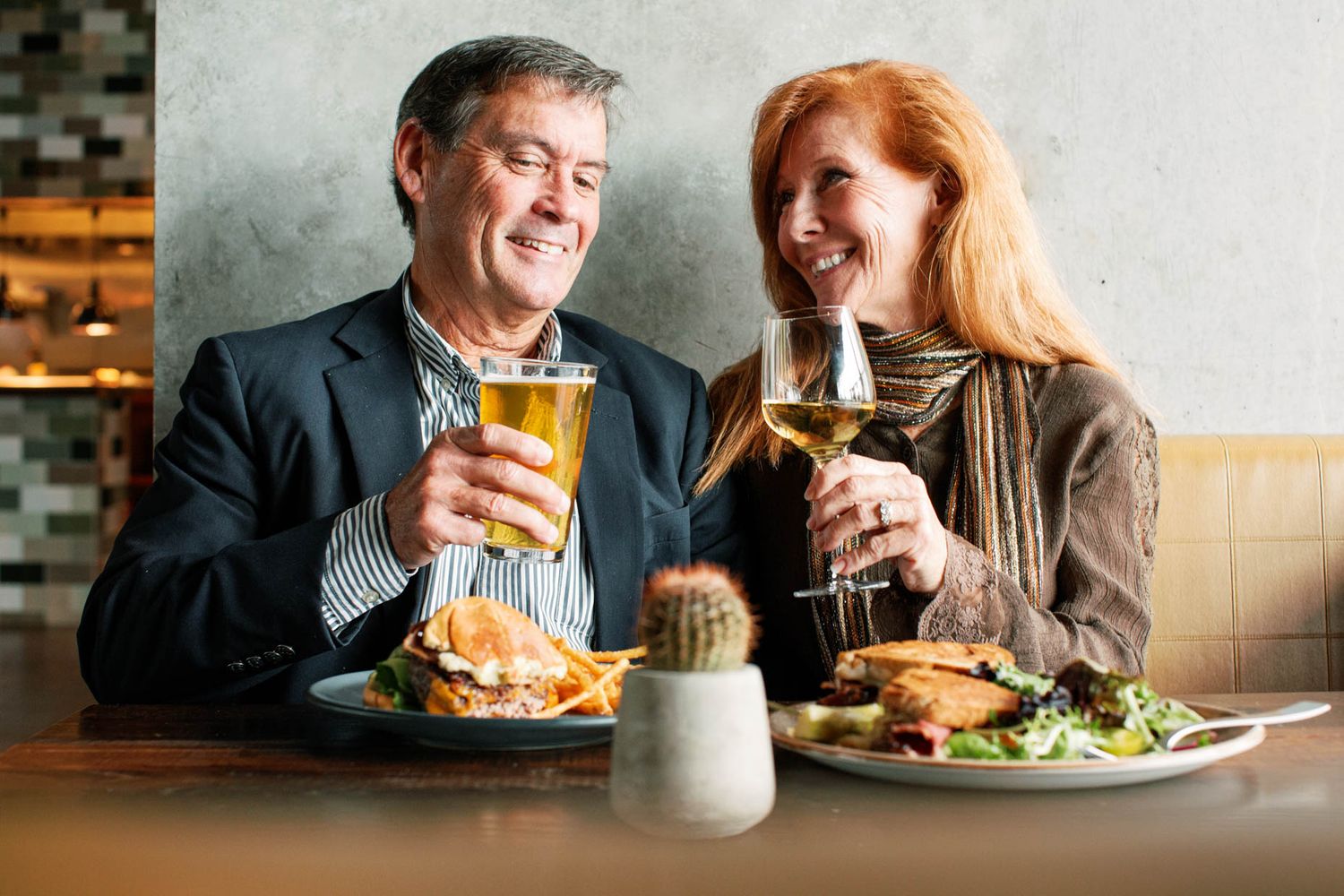 Middle-aged couple enjoying lunch with beer and wine at a restaurant, smiling and toasting together.