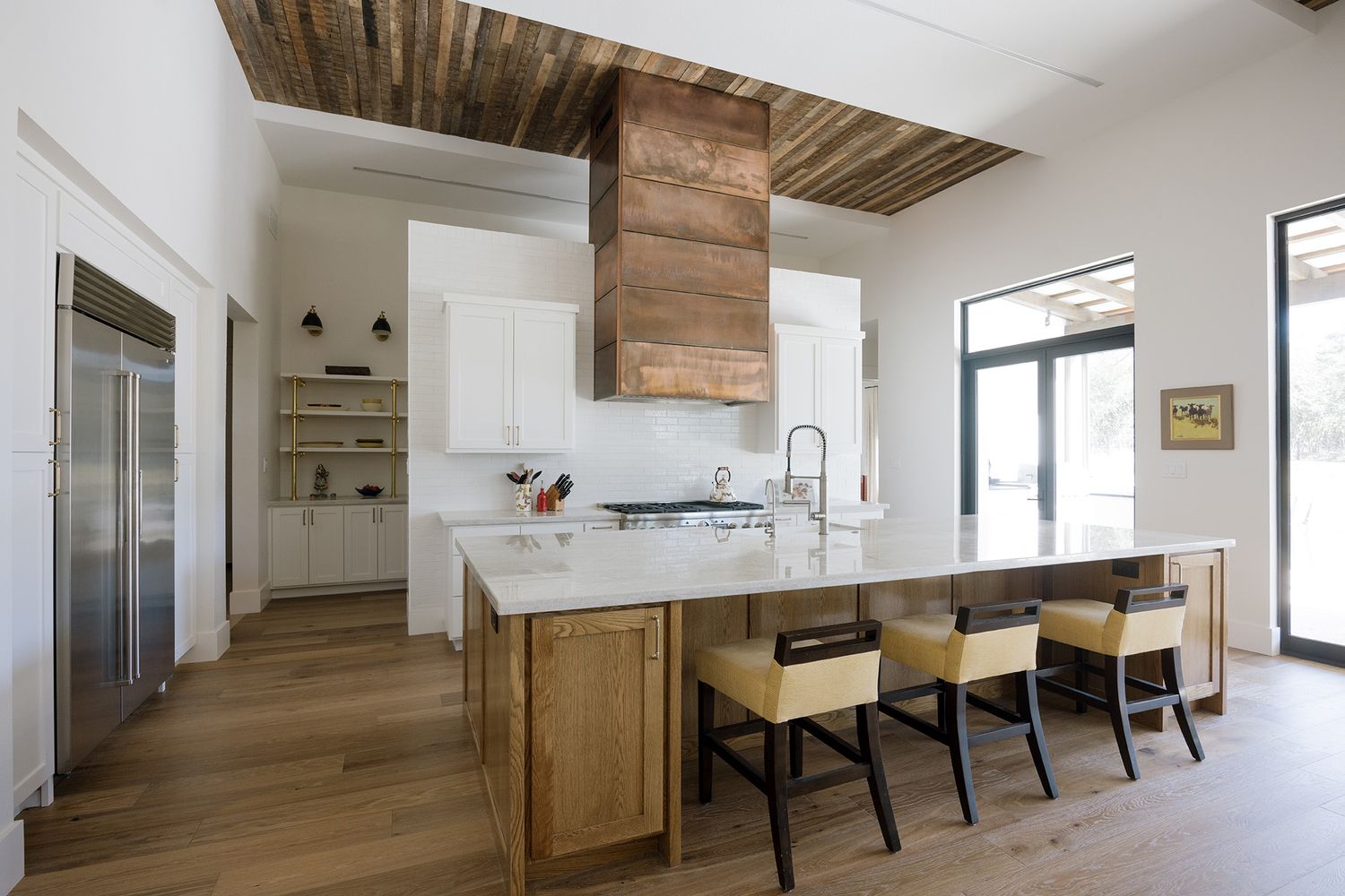 Modern kitchen with wood island, white cabinets, reclaimed wood ceiling, and bar seating under natural light.