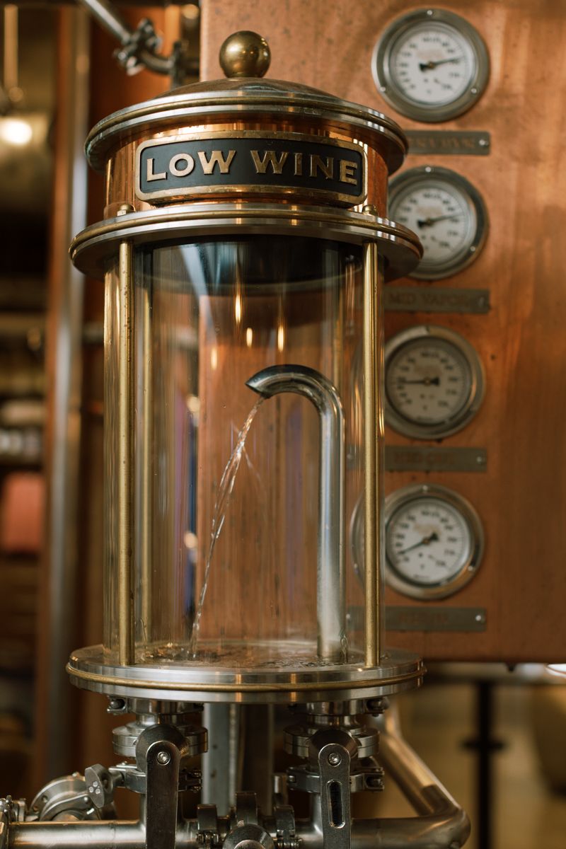 Brass low wine spirit safe with glass cylinder and pressure gauges at a distillery.