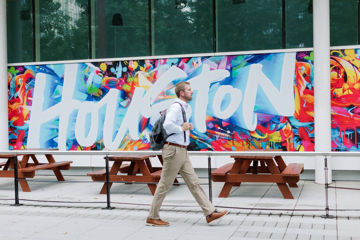 Man walking past a vibrant Houston mural sign outside a modern urban building.