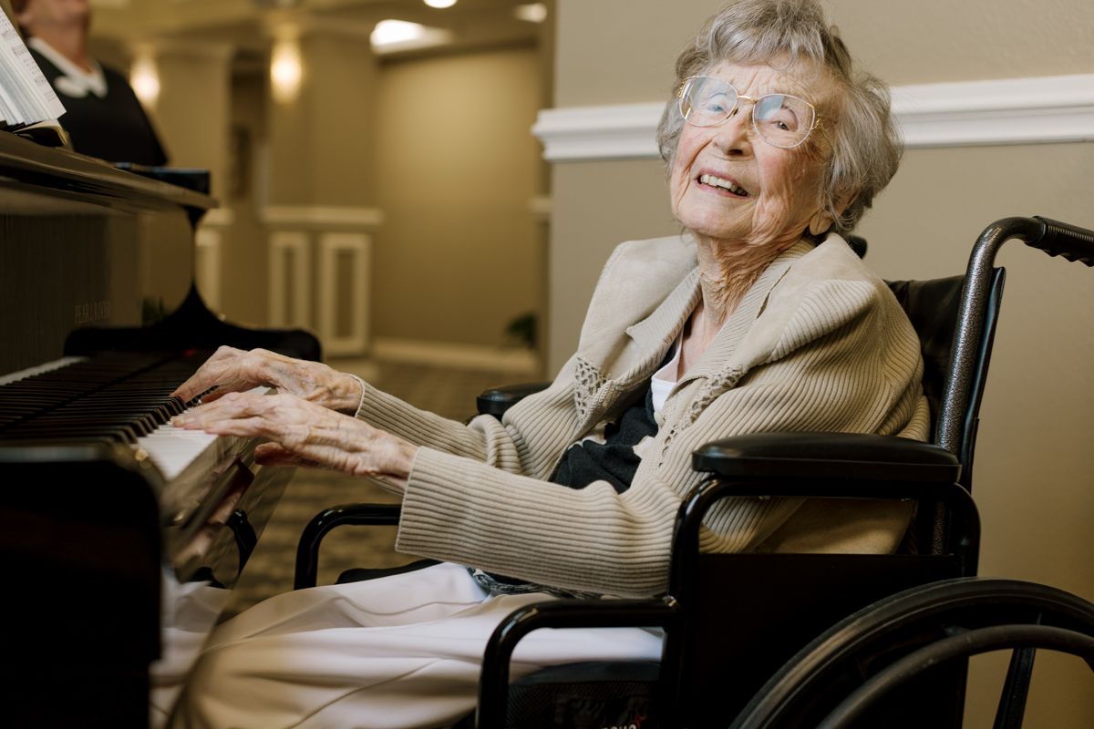 Happy elderly woman in wheelchair playing piano with joy at a senior living facility.