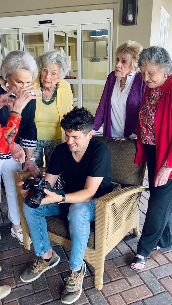Photographer shows camera preview to group of elderly women at an outdoor senior living facility.