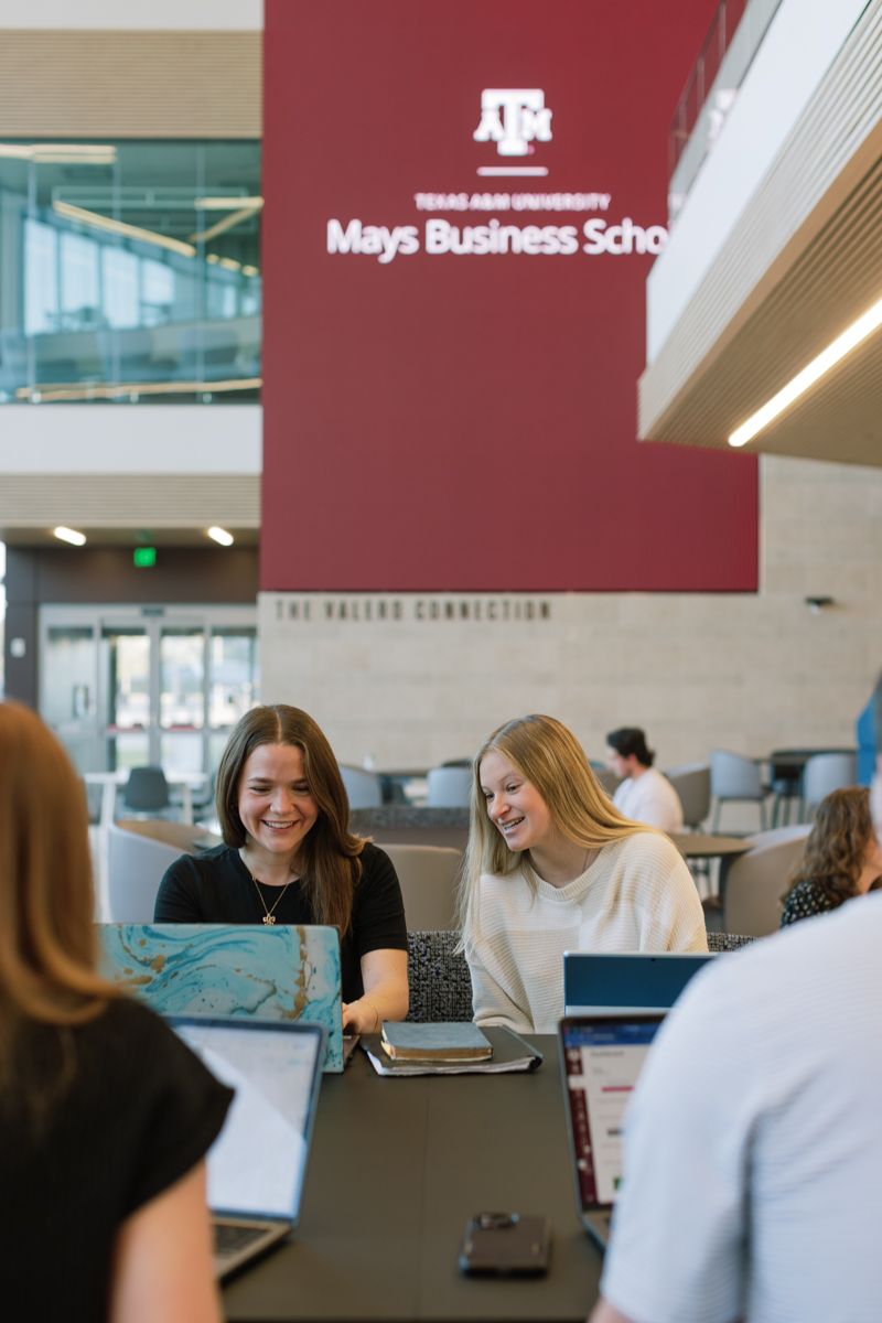 Two female students laughing and studying together at Texas A&M Mays Business School.