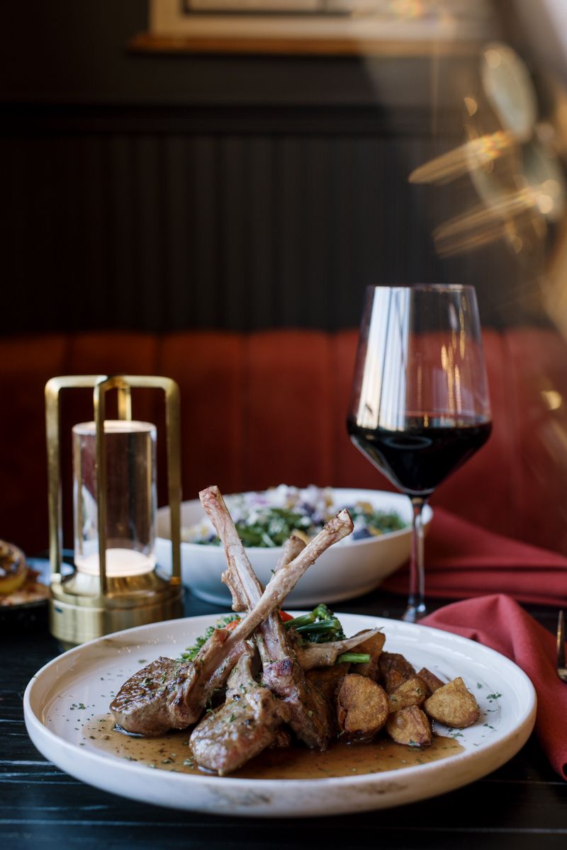 Elegant lamb chops with roasted potatoes on a white plate, served with red wine and candlelight in a upscale restaurant.