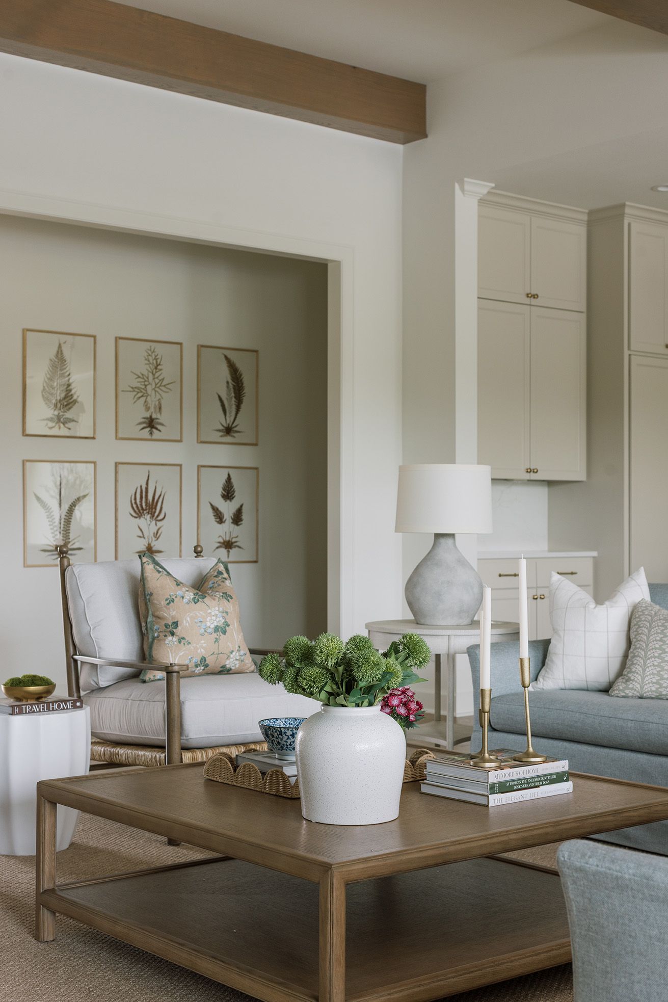 Coastal living room with botanical wall art, linen armchair, floral pillow, wood coffee table, and soft sage green accents.