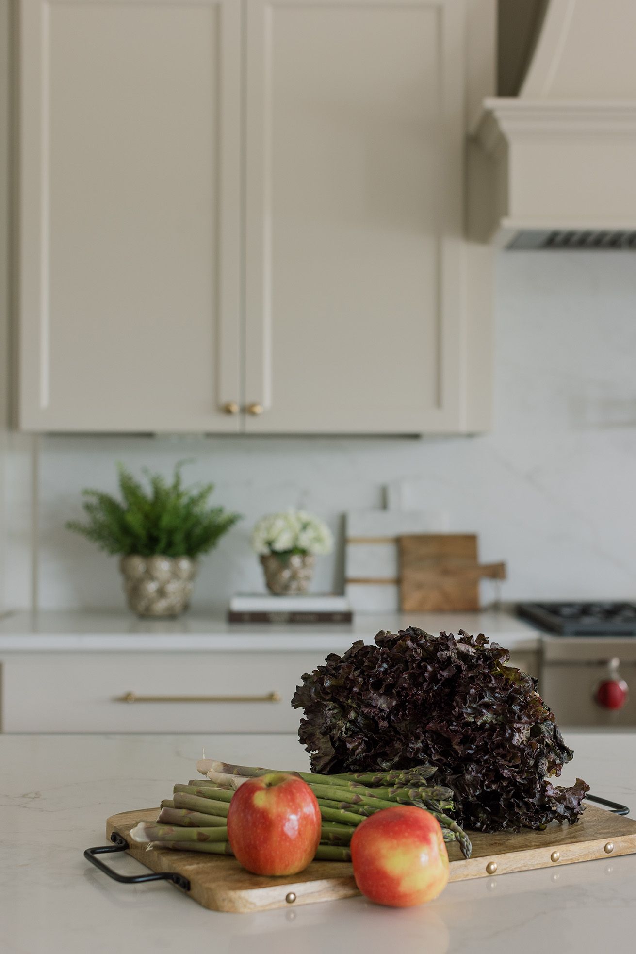 Bright kitchen counter with fresh produce including apples, asparagus, and red leaf lettuce on a wooden cutting board.