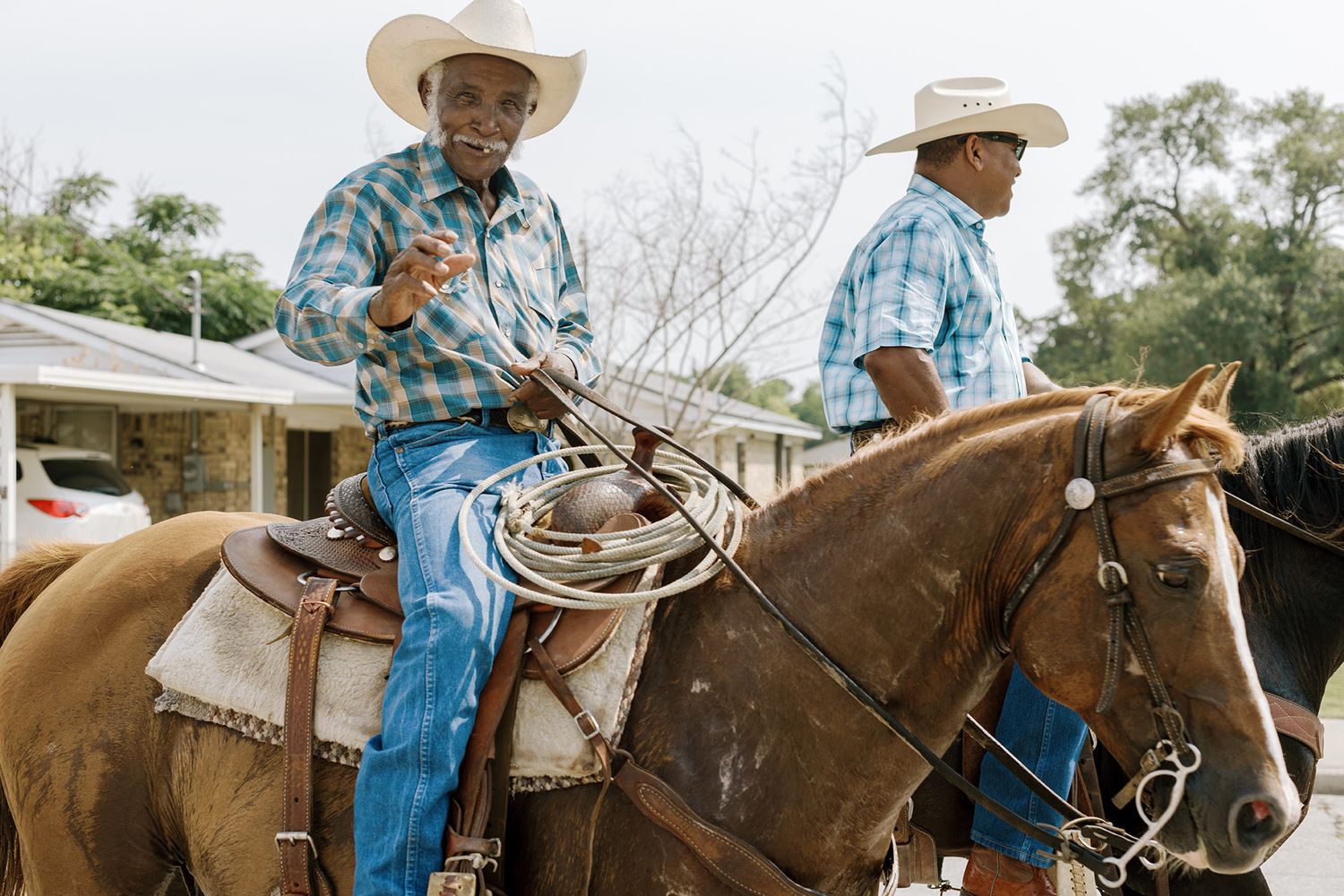 Two Black cowboys in cowboy hats ride horses while holding lasso ropes outdoors.