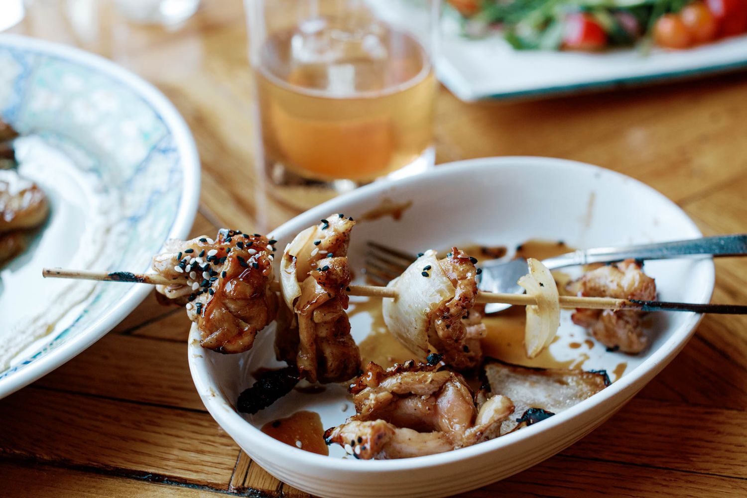 Grilled chicken skewers with sesame seeds served in a white bowl on a rustic wooden dining table.