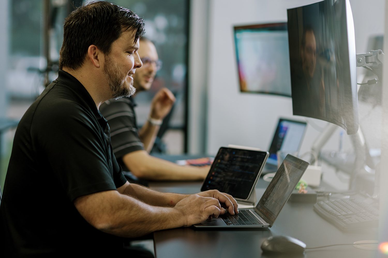 Two professionals working at computers in a modern office, focused on coding tasks with multiple monitors displaying data.