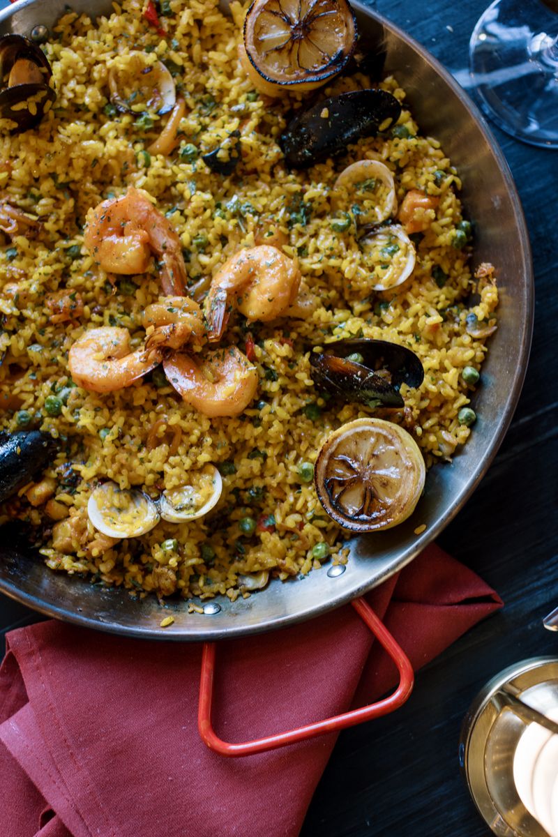 Seafood paella with shrimp, mussels, clams, and saffron rice garnished with grilled lemon in a traditional pan.
