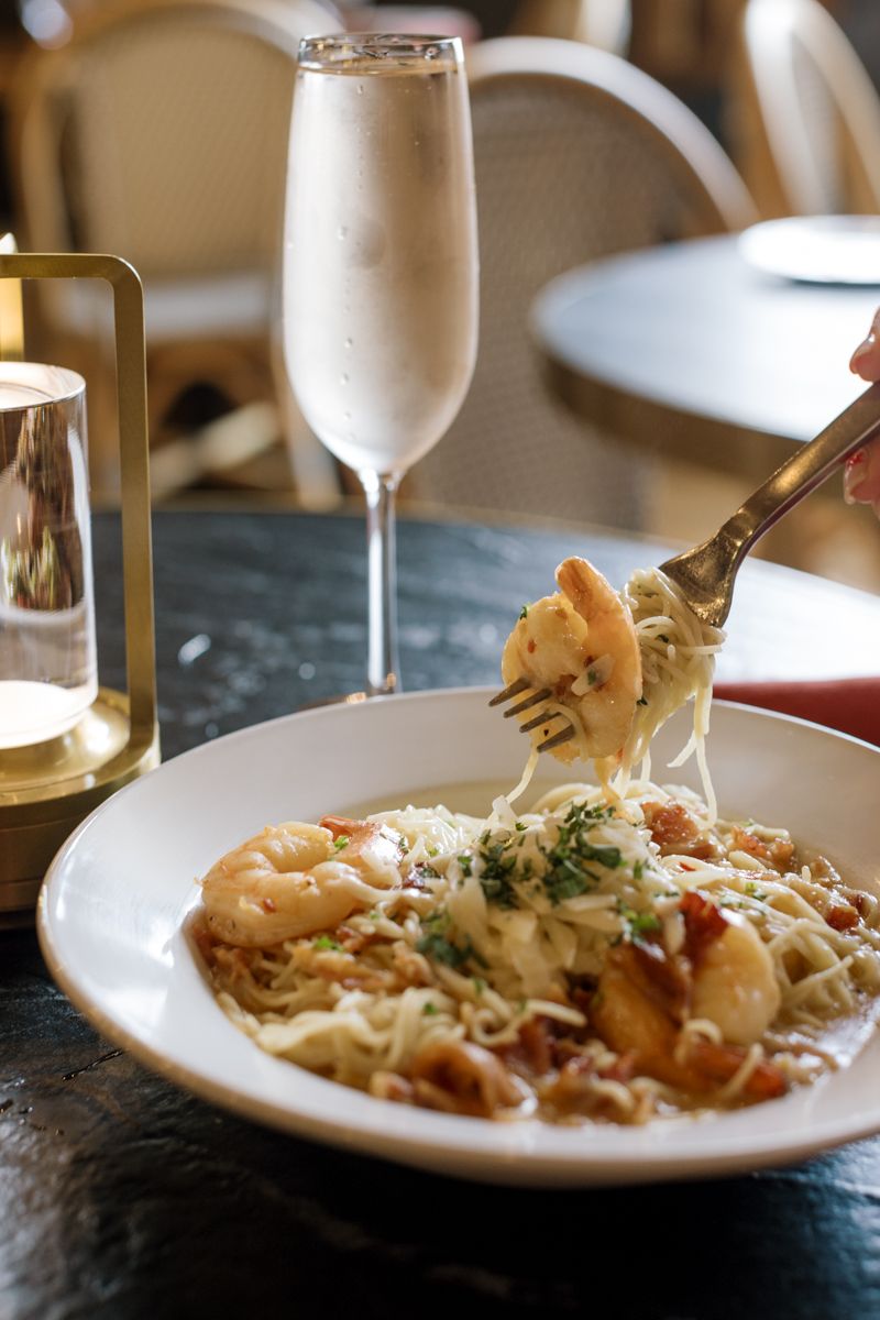 Shrimp pasta with creamy sauce on a white plate, fork twirling noodles, champagne flute and candle in background.