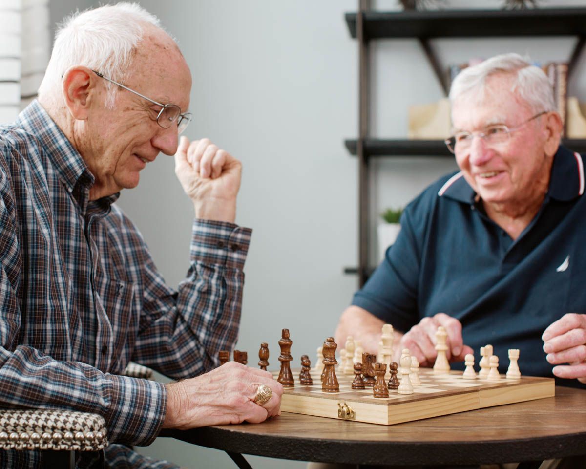 Two elderly men playing chess at a wooden table, smiling and engaged in a strategic board game.