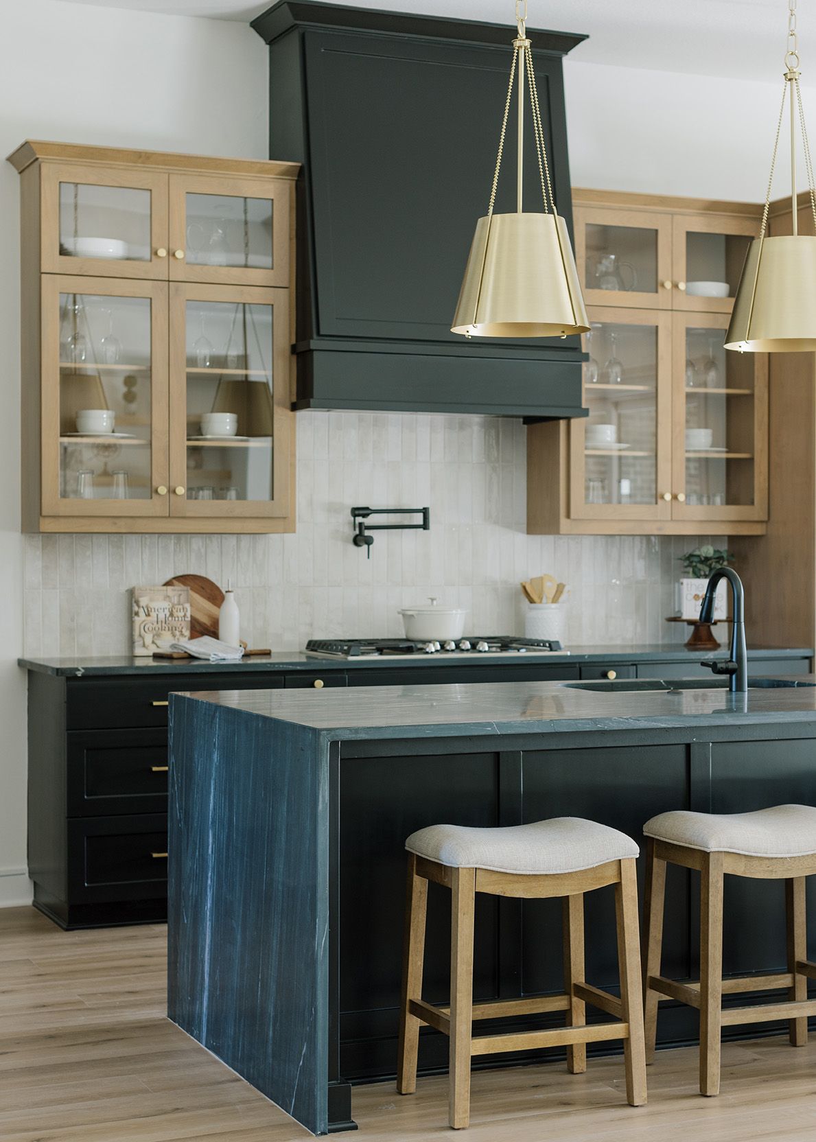 Two-tone kitchen with dark navy island, natural wood upper cabinets, brass hardware, and matching range hood.