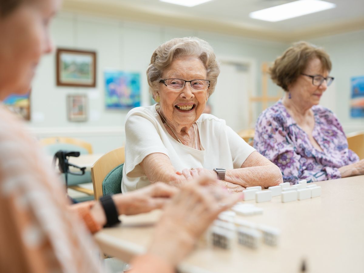 Happy elderly woman laughing while playing dominoes with friends at a community table.