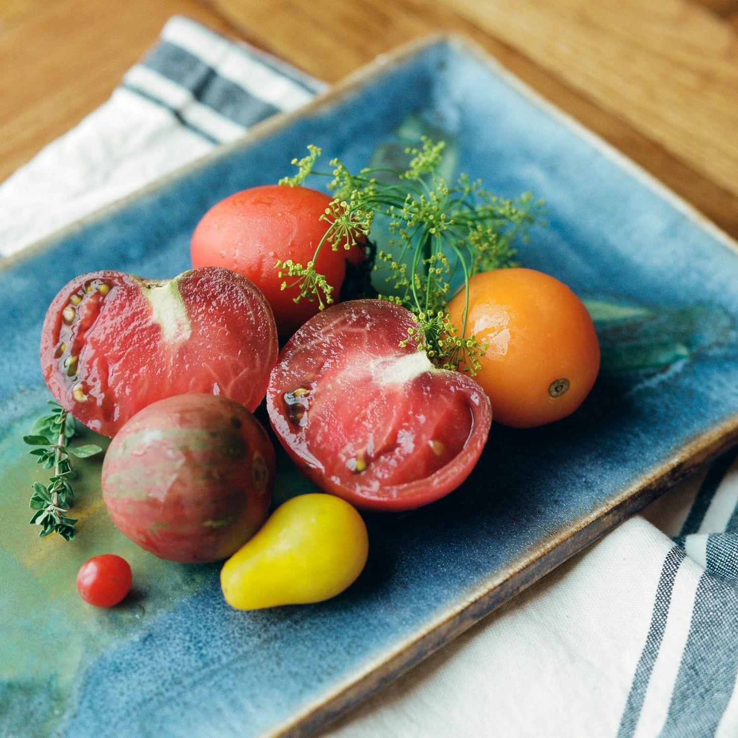 Colorful heirloom tomatoes with fresh herbs on a blue ceramic plate on a wooden table.