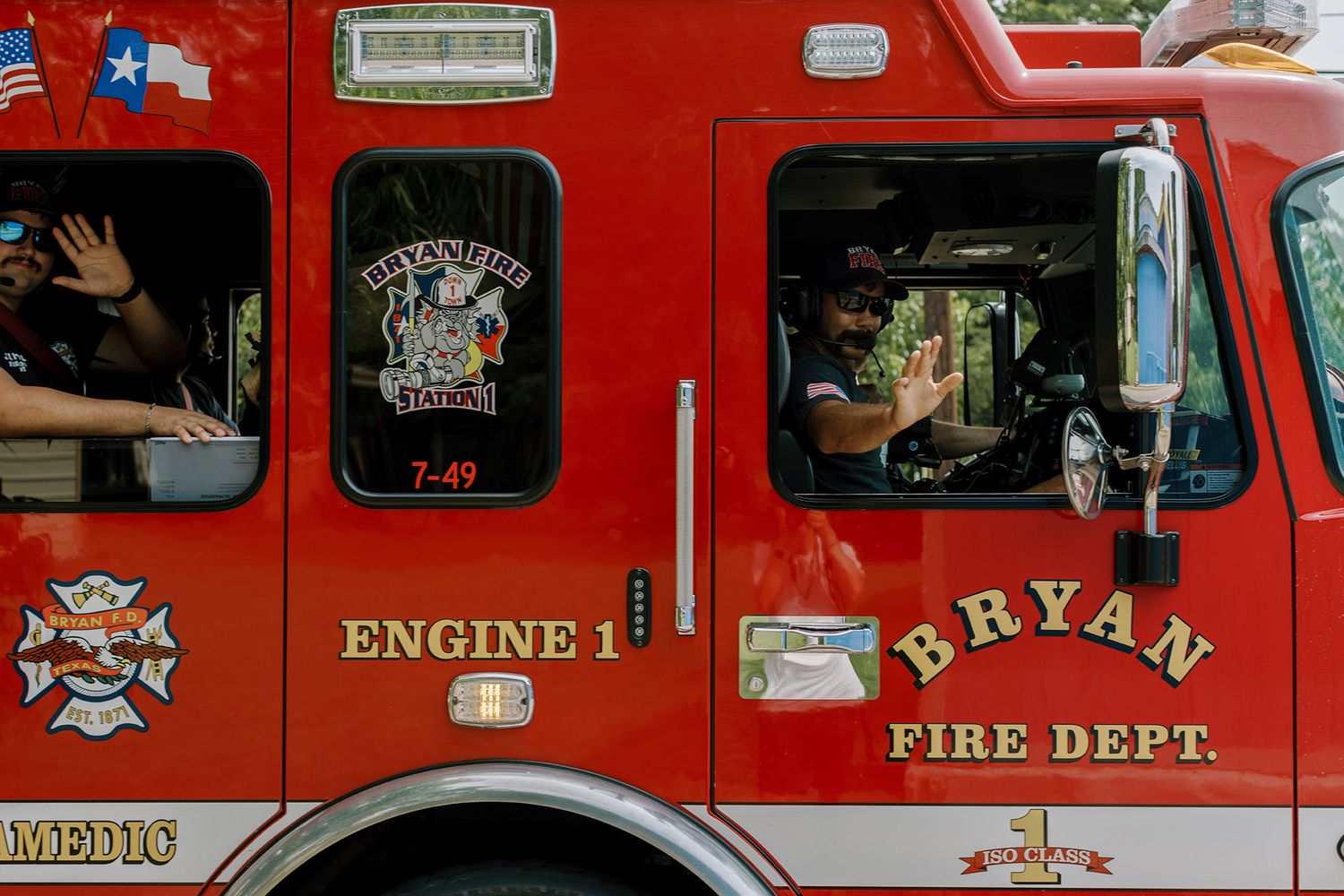 Bryan Fire Department Engine 1 paramedic red fire truck with firefighters waving from windows during a community event.