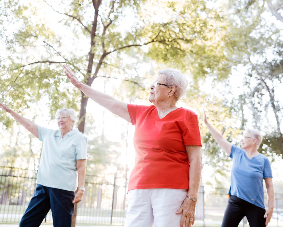 Active senior adults doing outdoor group exercise with arms outstretched in a sunny park.