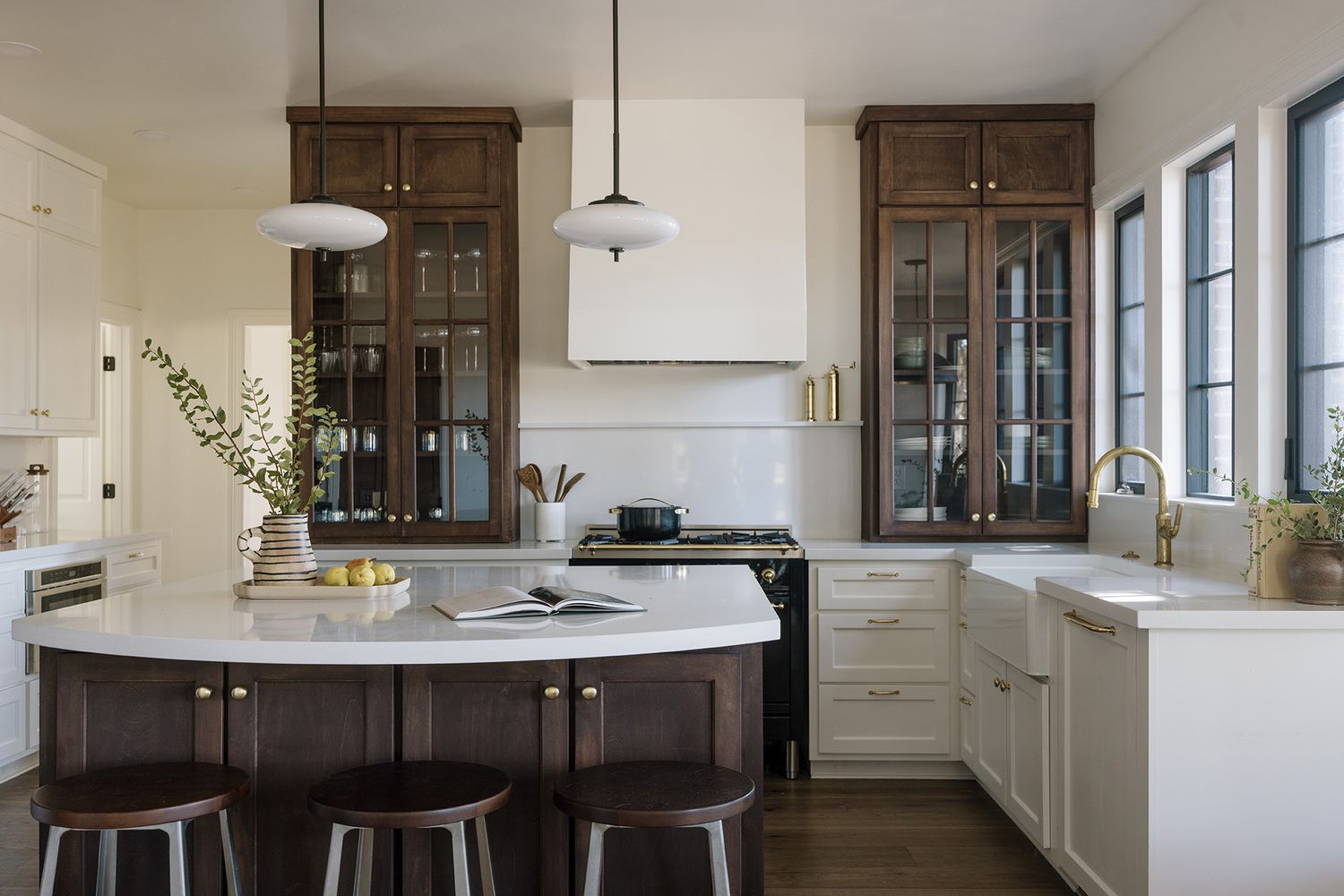 Elegant kitchen with dark wood glass-front cabinets, white hood, marble island, and gold fixtures.