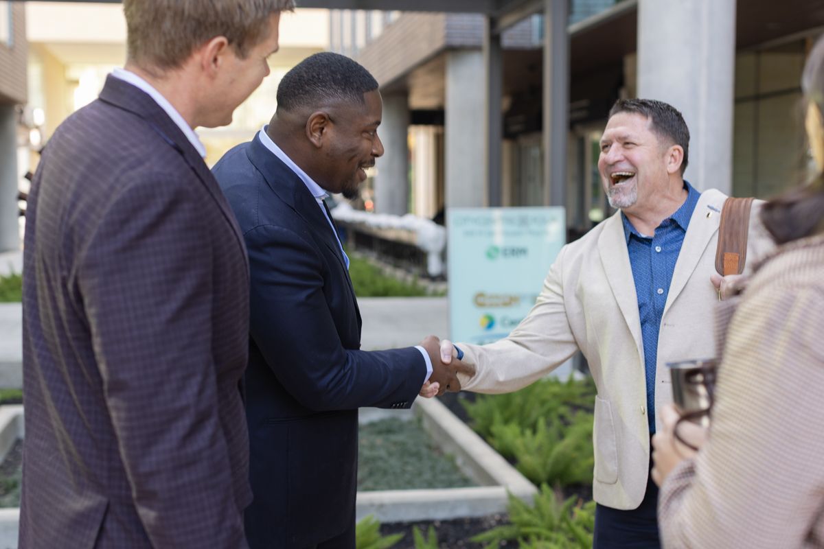 Business professionals shake hands and smile during a networking event outside.