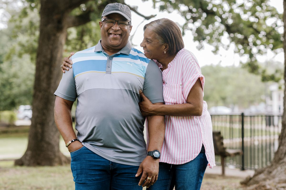 Happy older couple embracing and smiling outdoors under a large tree.