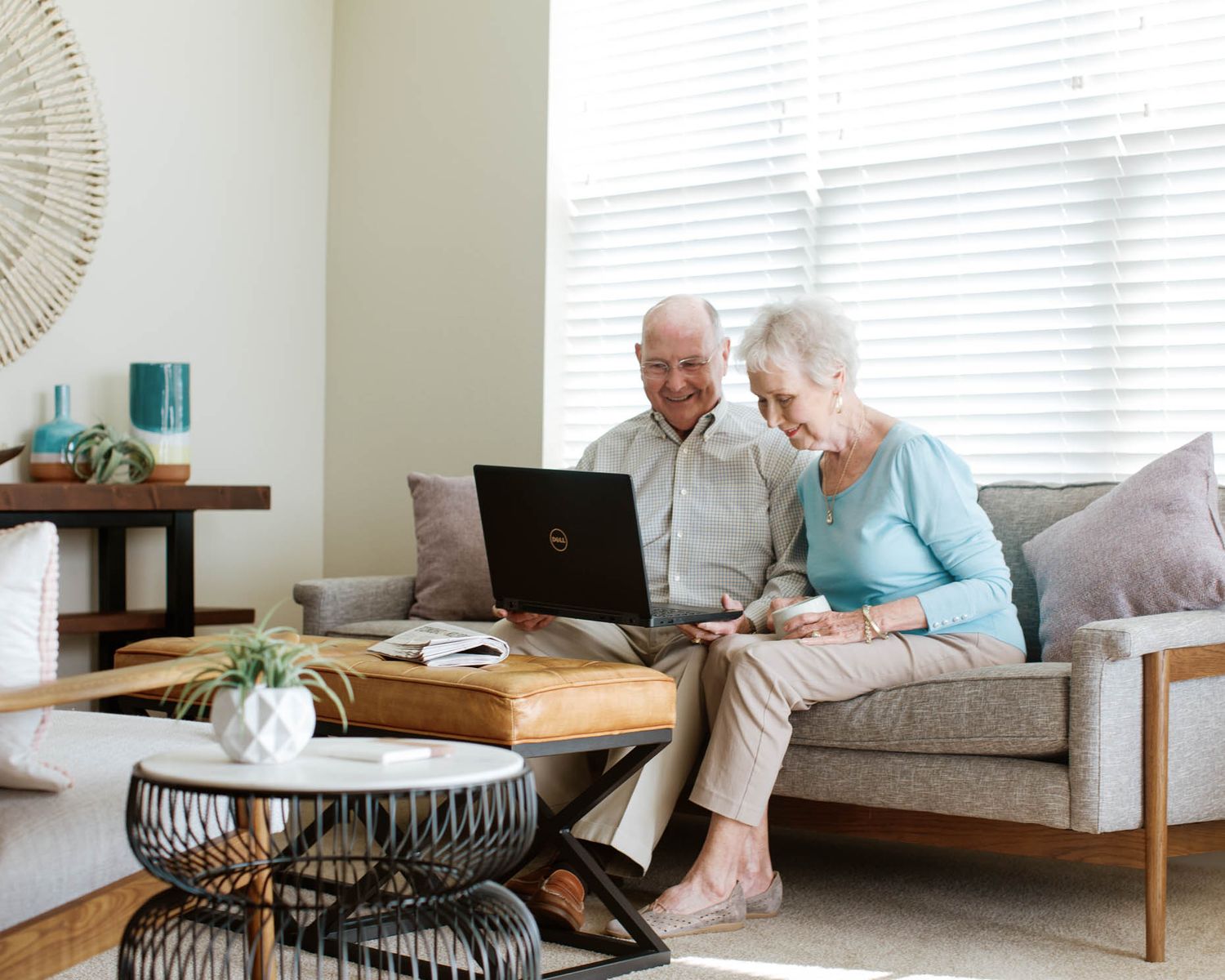 Elderly couple smiling and using a Dell laptop together on a couch in a bright, modern living room.