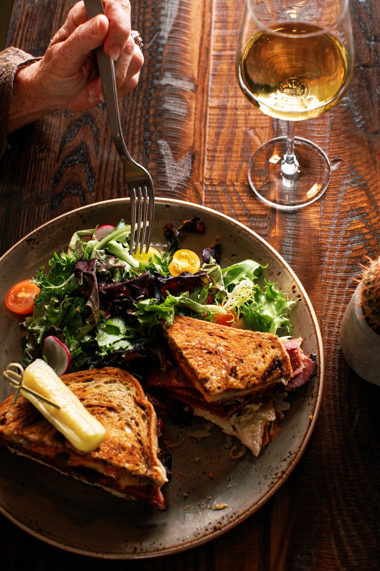Grilled sandwich with fresh garden salad on rustic plate, paired with white wine on wooden table.