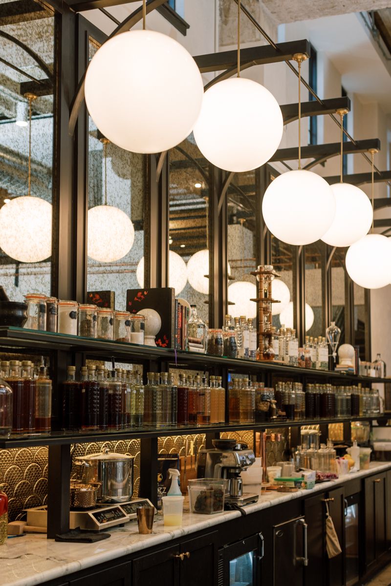Elegant bar counter with globe pendant lights, mirrored shelves, and rows of ingredient jars.