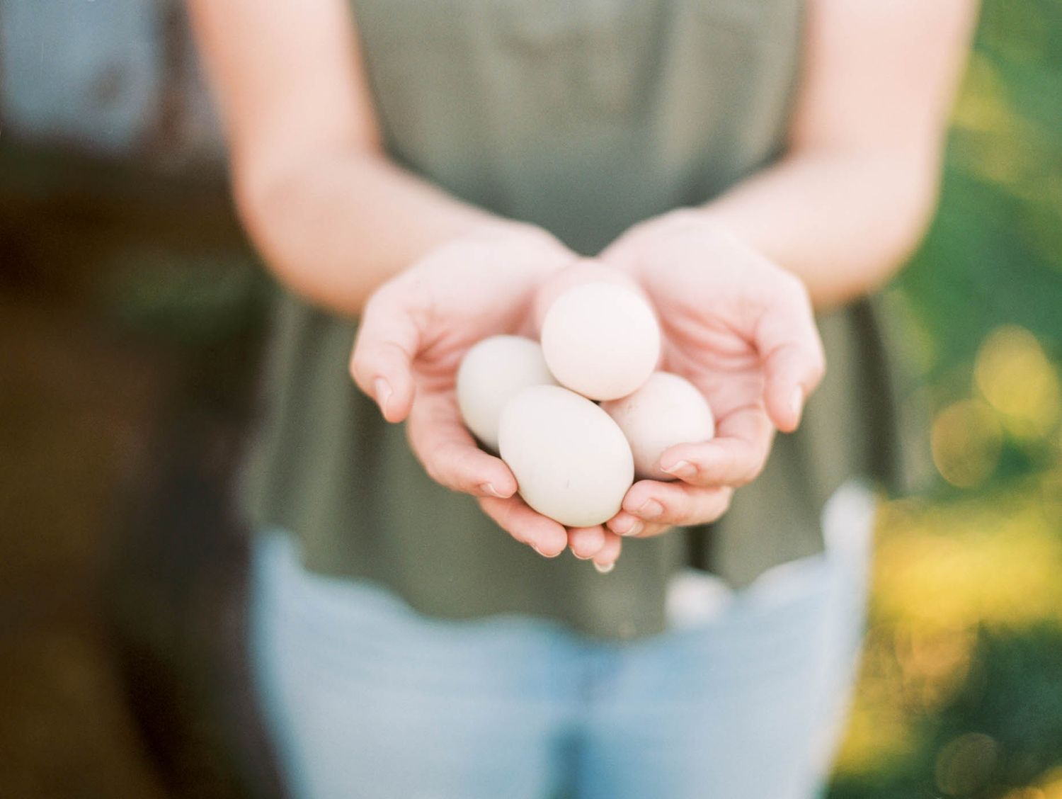 Woman holding three fresh white farm eggs in her cupped hands outdoors.