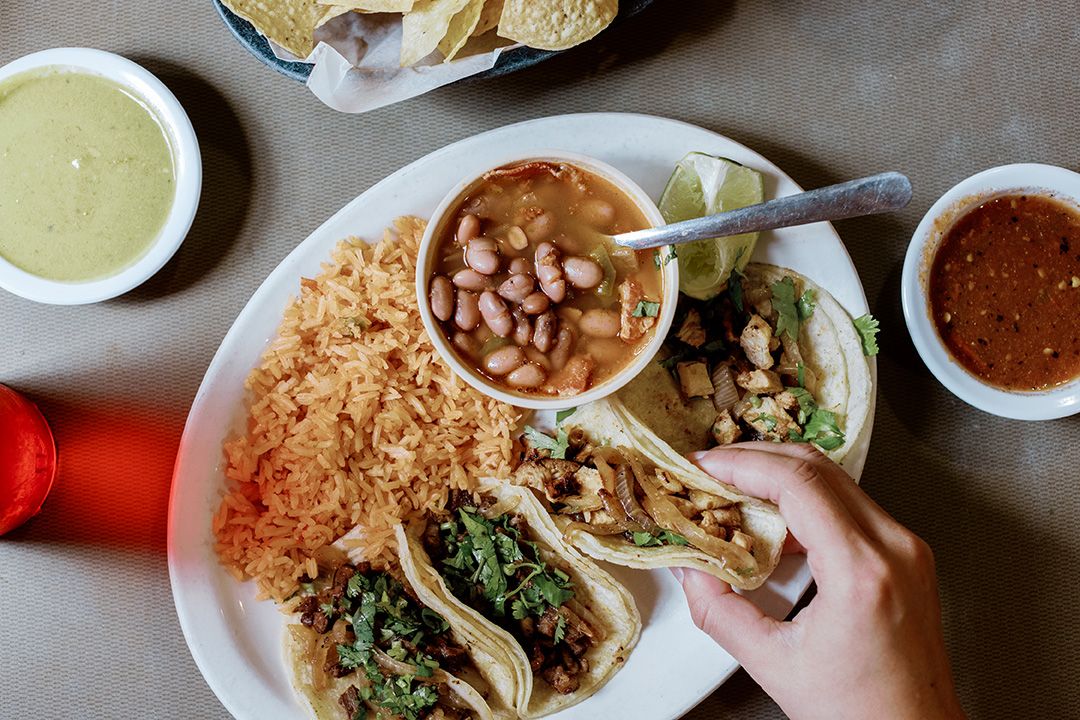 A plate of street tacos with rice, beans, and salsas at a Mexican restaurant.