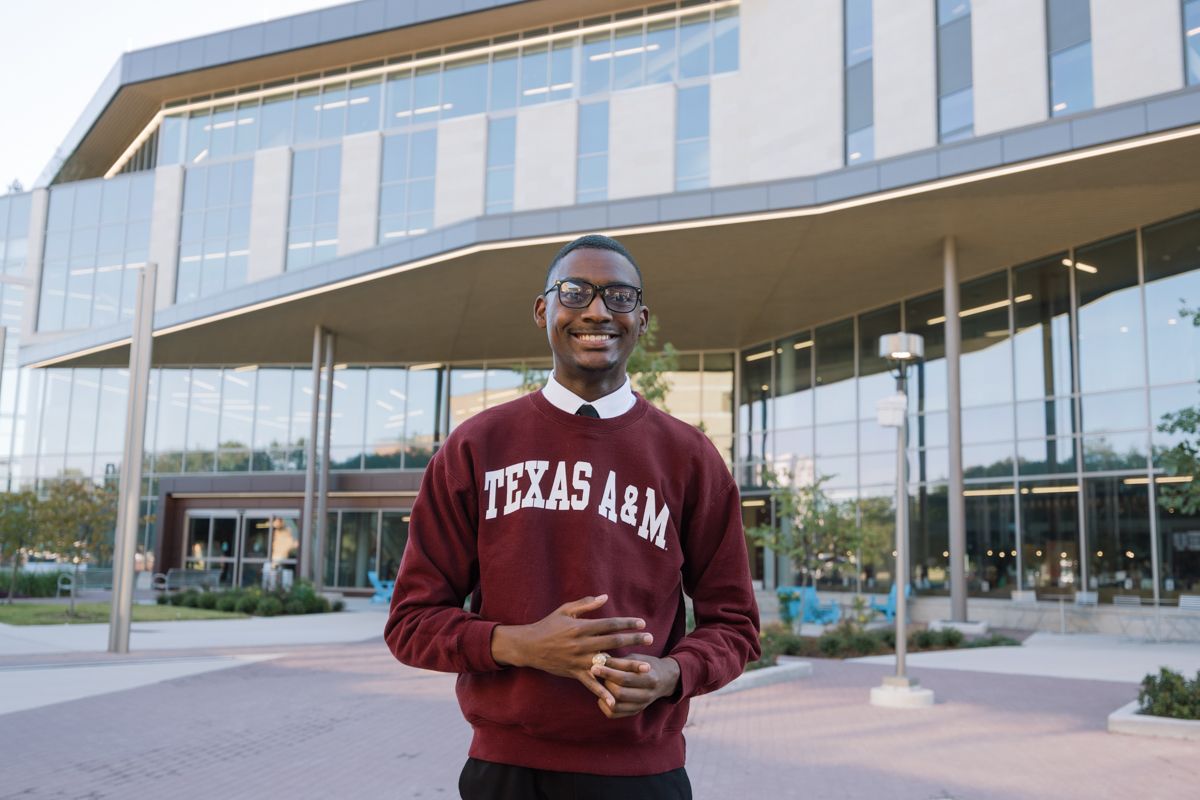 Male student wearing Texas A&M sweatshirt standing outside a modern university building.